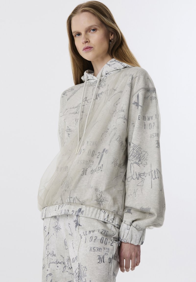 Hoodie gris clair avec des motifs abstraits gris, capuche à cordon et poignets élastiques. Fabriqué à partir d'un tissu doux avec une légère superposition transparente.