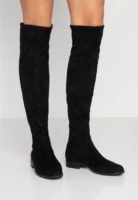 Stivali neri al di sopra del ginocchio realizzati in morbido camoscio, con design aderente, punta rotonda, tacco basso a blocco e cuciture minimaliste.