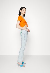 Top cropped laranja brilhante com tecido texturizado, combinado com jeans de cintura alta azul claro e sandálias de salto azuis.