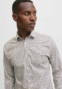 Camicia bianca con bottoni, caratterizzata da un denso motivo floreale multicolore. Presenta un colletto classico e un design aderente. Tessuto dalla texture liscia.