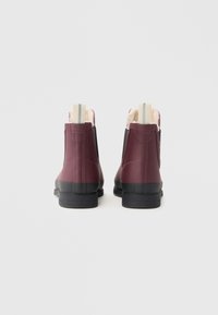 Bottes en caoutchouc bordeaux avec une texture lisse, semelles noires et doublure en peluche, dotées d'une languette beige avec deux rayures.