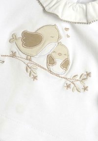 Top in tessuto bianco con uccelli ricamati in beige su un ramo con foglie. Collo a balze con cuciture decorative.