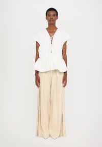 White, short-sleeve top with gathered detailing and drawstring neckline, paired with flowy, beige, high-waisted wide-leg trousers.