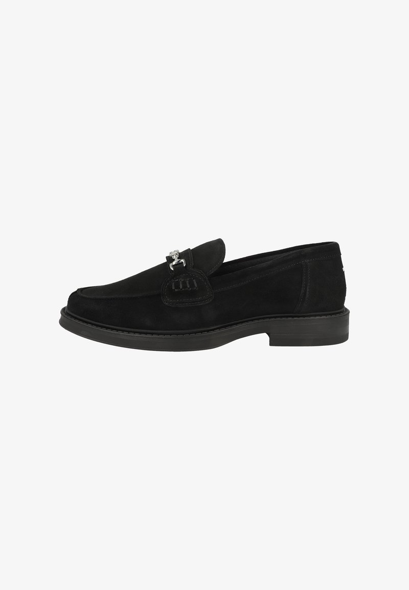 Zapato negro de ante sin cordones con puntera redondeada, suela plana y acento decorativo de hardware plateado en la parte delantera. Textura suave y diseño clásico.