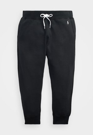 Pantalon de survêtement noir en tissu doux, doté d'une taille élastique avec un cordon blanc et des poignets côtelés. Logo sur la cuisse gauche.