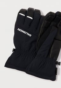 Musthave ja tumesinised kindad venitusmaterjalist mansetiga, kummist aktsentidega sõrmedel ja valge logo. Reguleeritav rihm randmel.