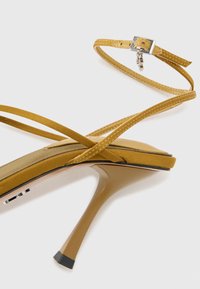 Sandale à talon haut jaune avec une fine lanière à la cheville, semelle intérieure rembourrée et talon aiguille brillant. Design texturé au niveau des orteils.
