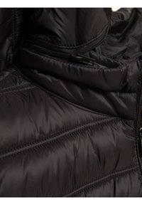 Tuvaikta melna izšūta jaka, kas rāda pildīta auduma struktūru, diagonālas šuves un daļēji atvērtu rāvējslēdzēja kabatu.