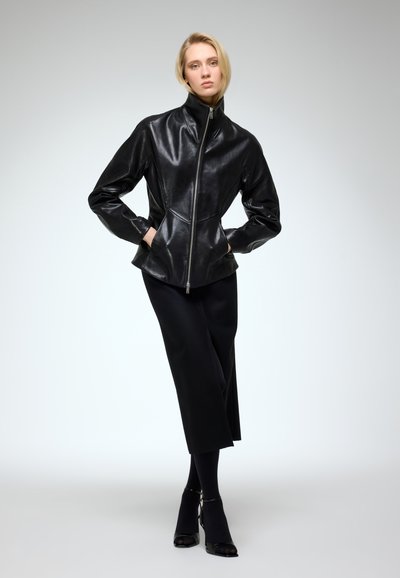 Black leather jacket with high collar, zip closure, and loose fit. Paired with a black skirt and tights, worn over black high-heeled shoes.