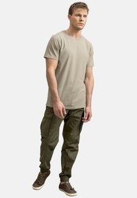 Beige T-shirt met korte mouwen, gecombineerd met groene cargobroek met zakken en boorden. Bruine sneakers met veters maken de outfit af.
