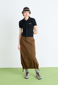 Camisa polo preta de mangas curtas com botões, combinada com uma saia maxi castanha. Acentuada com um chapéu de balde estampado e ténis multicoloridos.