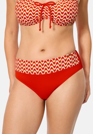 Mujer con un top de bikini rojo y blanco con estampado y braguitas de bikini rojas a juego de talle alto.