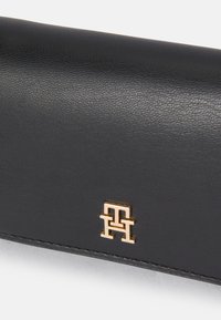 Portofel din piele neagră cu finisaj texturat, având un emblemă cu logo în nuanță de aur. Design compact cu linii curate și fără accesorii suplimentare.