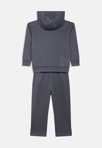 Ensemble sweat-shirt et pantalon gris, fabriqué en tissu lisse. Comprend une capuche, des manches longues et une ceinture élastique avec une coupe décontractée.