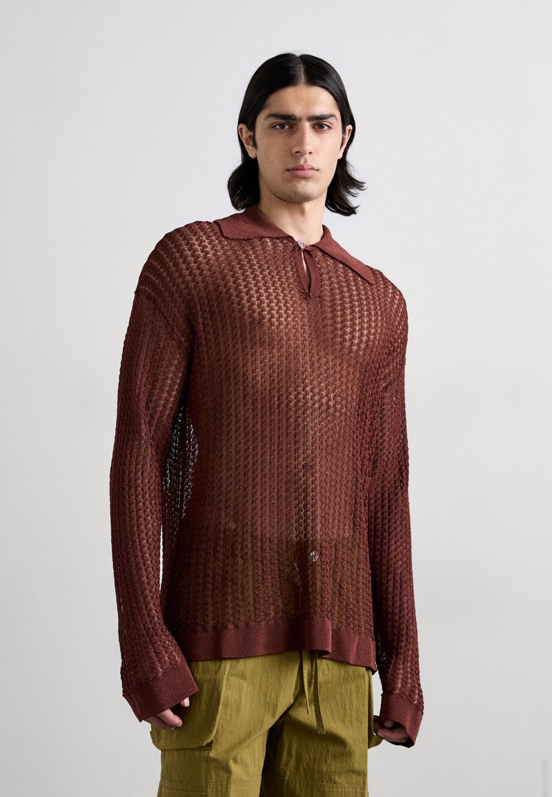 Maglione a rete marrone con colletto e dettaglio cravatta, caratterizzato da maniche lunghe e una vestibilità ampia. Abbinato a pantaloni cargo verde oliva.