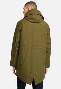 Olivgrön vattentät jacka med huva, dragkedja framtill och tryckknappar vid fållen, med en delad design på baksidan.