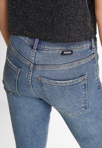 Hög midja blå jeans i denim, med en klassisk femfickdesign, avslöjad sömnad och ett märkesetikett bak.