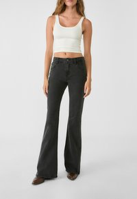 Jeans neri a zampa d'elefante con design a cinque tasche e un fitted crop top bianco con scollatura a girocollo e spalline sottili.
