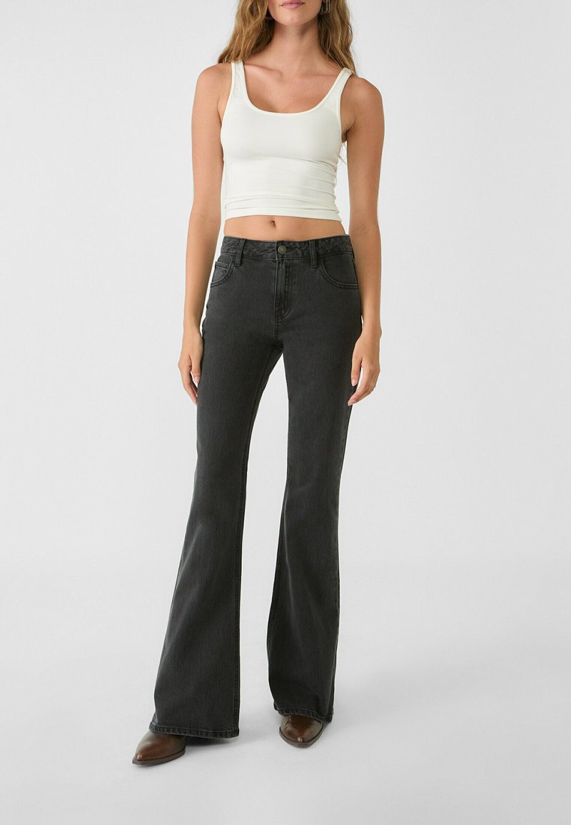 Jeans neri a zampa d'elefante con design a cinque tasche e un fitted crop top bianco con scollatura a girocollo e spalline sottili.
