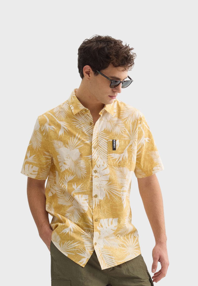 Kortarmige button-up shirt in geel met een wit tropisch bladdessin, voorzien van een borstzak aan de linkerkant en een merklabel op de zak.