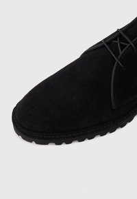 Scarpa in suede nero con punta arrotondata, design con lacci e suola in gomma testurizzata. Caratterizzata da cuciture minime e finitura opaca.