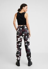Svart ribbet crop topp paret med grå, hvite og burgunder camo joggebukser. Joggebuksene har elastiske mansjetter og sidelommer. Kraftige svarte støvler.