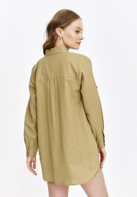 Khaki koszula zapinana na guziki z tylnym karczkiem, długimi rękawami i zaokrąglonym dołem; wykonana z lekkiego, strukturalnego materiału.