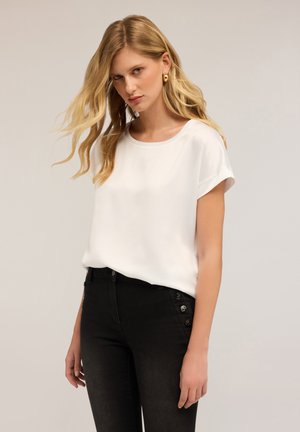 Witte blouse met korte mouwen en een ronde halslijn, met een gladde textuur, gecombineerd met strakke zwarte jeans met knoopaccenten aan de zijkant.
