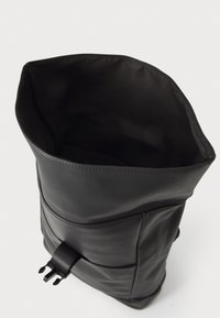 Svart skinnryggsekk med rulltopdesign, jevn tekstur og en frontlomme. Har en solid stropp og minimalistisk stil.