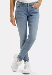 Jasnoniebieskie cienkie dżinsy wykonane z denimu, z pięcioma kieszeniami, klasycznym stanem i subtelnym wybłyszczeniem. Połączone z białymi butami sportowymi.