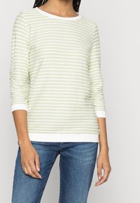 Haut vert clair à manches longues avec rayures blanches, col rond et poignets blancs. Associé à un jean en denim bleu.