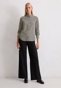Chemise à boutons en motif géométrique noir et blanc, à manches longues, associée à un pantalon large taille haute noir et des chaussures brillantes noires.