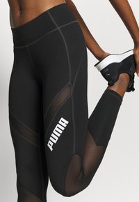Svarta leggings med meshpaneler, elastisk midja, kontrasterande grå sömmar och en framträdande vit "PUMA"-logotyp på sidan.