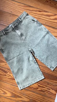 Lysegrå acid-wash denimshorts med frontlommer og beltehemper liggende flatt på et tregulv.