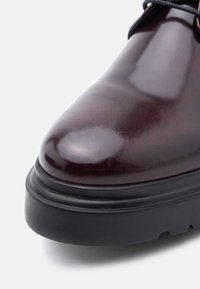 Μπορντό γυαλιστερό δερμάτινο παπ ούτσι με στρογγυλεμένη μύτη, μαύρη ελαστική σόλα και λεία υφή, με διακριτική λάμψη και μινιμαλιστικό σχεδιασμό.