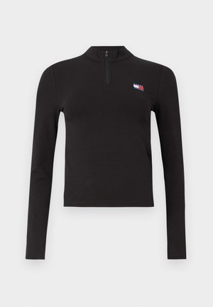 Zwarte langmouw crop top met een kwart rits en klein rood, wit en blauw Tommy Jeans-logo op de linkerborst, tegen een witte achtergrond.