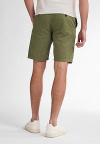 Olive green cotton shorts with rolled hems, side pockets, and two back pockets, paired with light-colored sneakers.