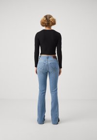 Blå utsvängda jeans med hög midja, femficksdesign och zickzacksting på bakfickorna. Matchas med en svart långärmad topp.