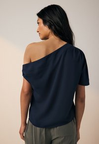 Navy blue off-the-shoulder top with short sleeves, smooth texture, and a curved hem. Lightweight fabric drapes loosely around the body.