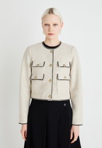 Geknipte beige wollen jas met zwarte rand, voorzien van gouden knopen en twee voortassen, gecombineerd met een zwarte rok. Vlotte textuur, op maat gemaakte pasvorm.