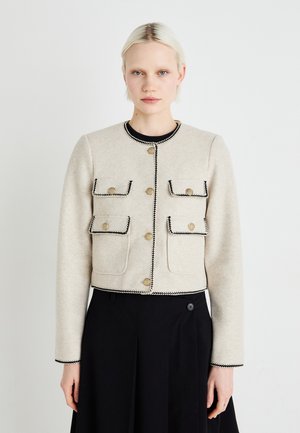 Geknipte beige wollen jas met zwarte rand, voorzien van gouden knopen en twee voortassen, gecombineerd met een zwarte rok. Vlotte textuur, op maat gemaakte pasvorm.