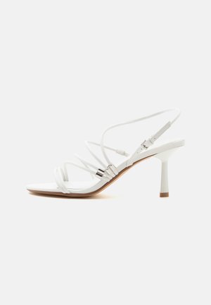 Sandale blanche à talons hauts avec fines brides, accents argentés, bout carré et talon fin de hauteur moyenne sur fond blanc uni.