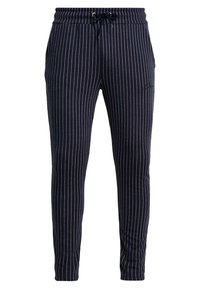 Námořnické modré slim-fit kalhoty s bílými vertikálními pruhy a černou tkaničkou v pase na bílém pozadí.