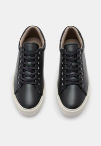 Schwarze Ledersneaker mit strukturierter Oberfläche, flachen schwarzen Schnürsenkeln, einer cremefarbenen Gummisohle und einem glatten beige Innenfutter.