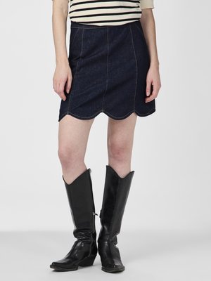 Jeans-A-Linien-Rock mit gewelltem Saum, der mit kontrastierenden goldenen Nähten verziert ist. Kombiniert mit kniehohen schwarzen Lederstiefeln mit spitzen Vorderteilen.