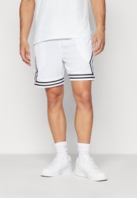 Hvide atletiske shorts med sorte sidelister, mesh-stoftekstur, over-knæ længde, parret med hvide sneakers og sokker.