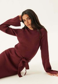 Bordeaux geribbelde gebreide jurk met lange mouwen en een strik taille detail, met een ronde hals en een gestructureerde stof. Een gladde afwerking overal.