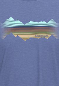 Camiseta azul con un gráfico de montaña multicolor con rayas en verde, marrón y azul. El nombre de la marca "Smartwool" está impreso en la parte inferior.