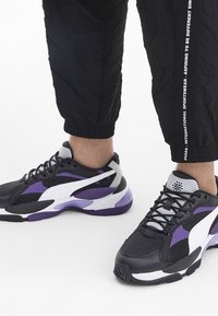 Schwarze und lila Sport Sneakers aus Netz- und synthetischen Materialien. Mit einer strukturierten Sohle, weißen Akzenten und einem niedrigen Schnitt.