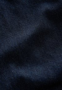 Gros plan d’un tissu en denim bleu foncé montrant un motif de tissage diagonal fin et des variations subtiles de texture.